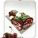 Chocolate Bûche de Noël cake decorated with holly, meringue, and powdered sugar, showing cherry and cream filling. Cherries a